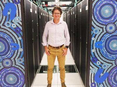 Professor Andy Hogg standing next to a blue supercomputer.